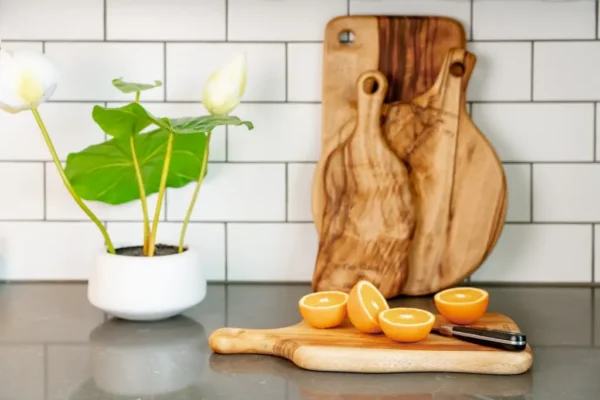 A cutting board with two wooden handles and three oranges on it.